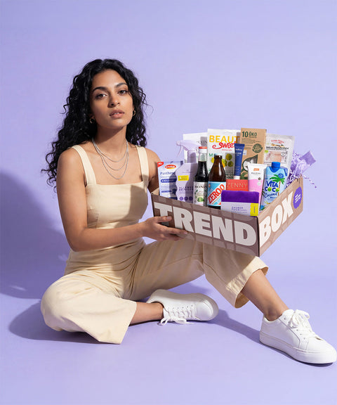 model mit juni trendbox auf dem knie, die trendbox ist gefüllt mit produkten aus den kategorien beauty& wellness lifestyle&design food&drinks, über 12 produkte insgesamt