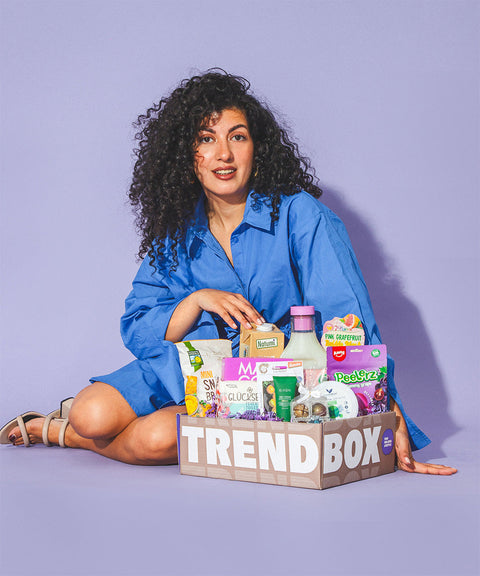 Frau mit lockigen Haaren und blauen Oberteil mit März Trendbox auf Lila Hintergrund