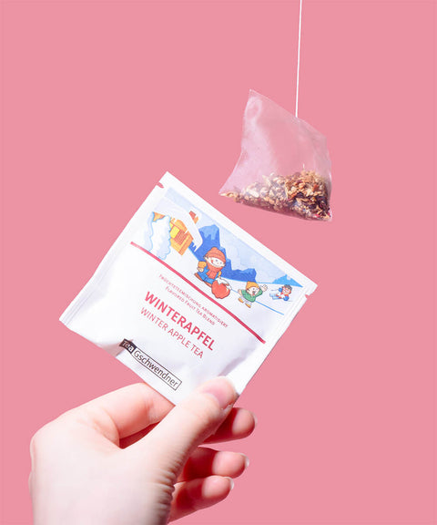 Teebeutel in der Hand vor rosa Hintergrund